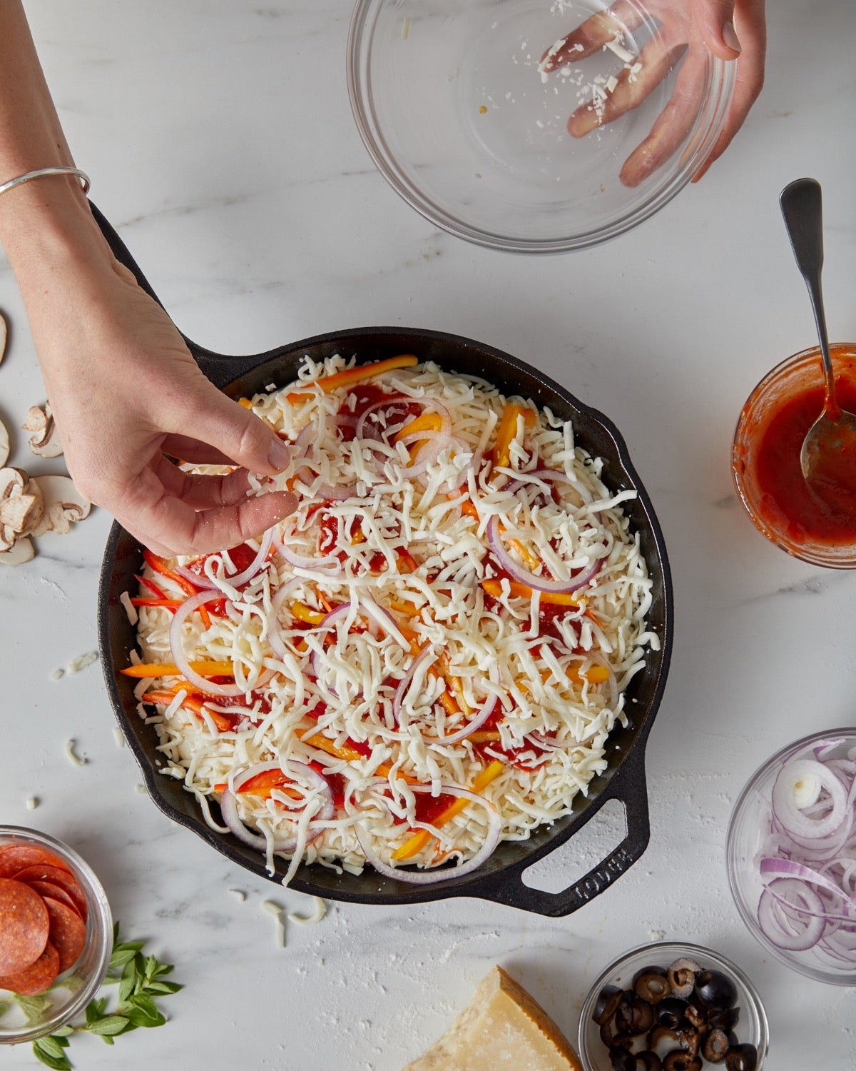 Cheese being sprinkled atop a pizza ready to go into the oven.